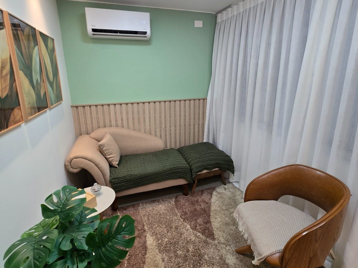 Consultório de psicoterapia com divã, poltrona e quadros de folhagem